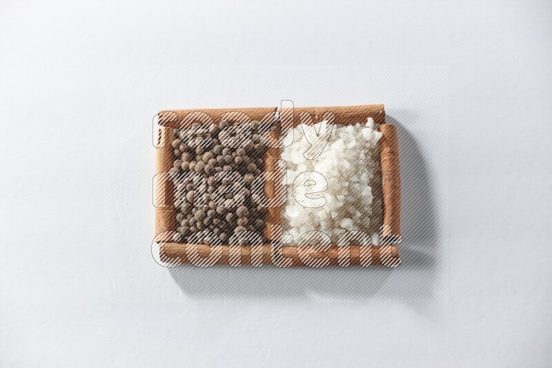 مربعان من أعواد القرفة ممتلئان بالملح الأبيض وحبوب الفلفل الحلو علي خلفية بيضاء