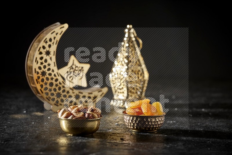 مكسرات في وعاء معدني مع المشمش المجفف بجانب فوانيس ذهبية علي خلفية سوداء