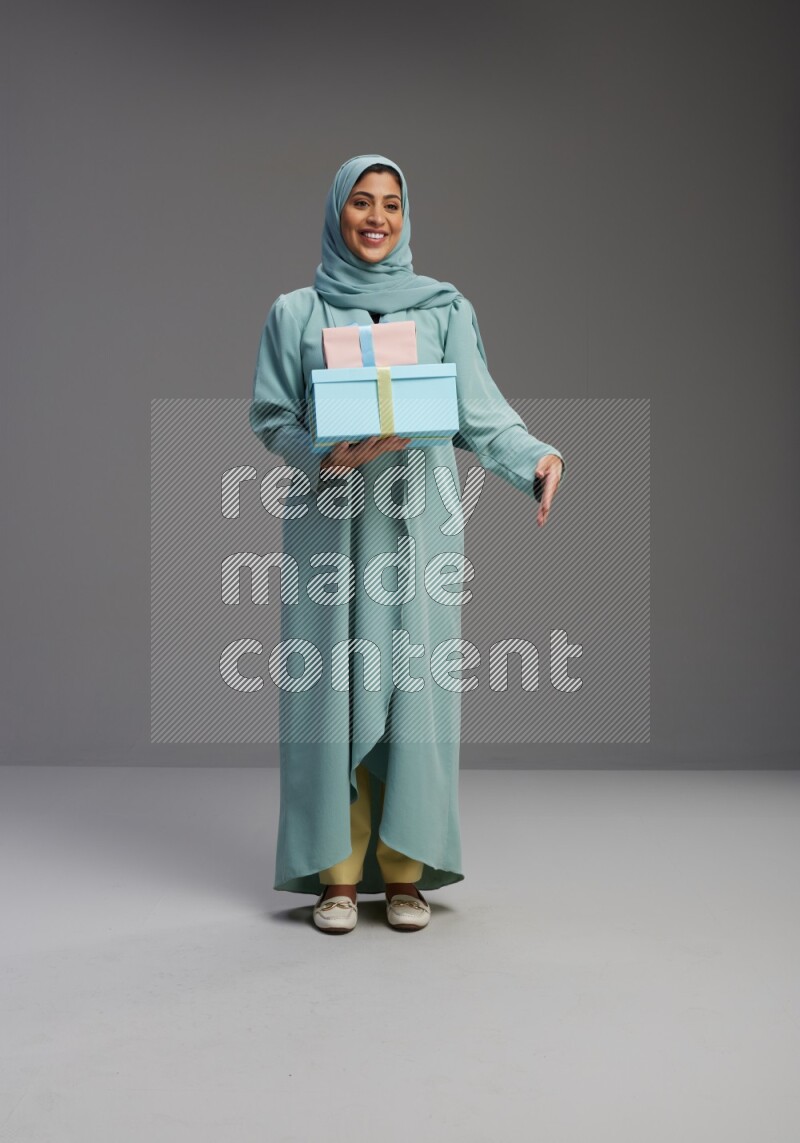Saudi Woman wearing Abaya standing holding gift box on Gray background