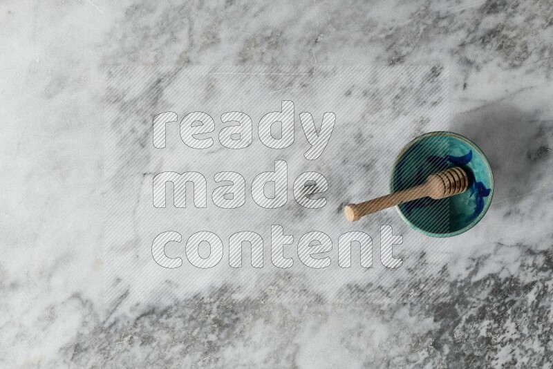 Decorative pottery bowl with wooden honey dipper in it on grey marble background