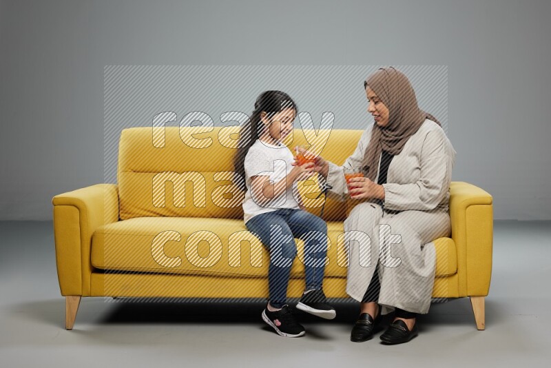 Mom and daughter sitting drinking juice on gray background