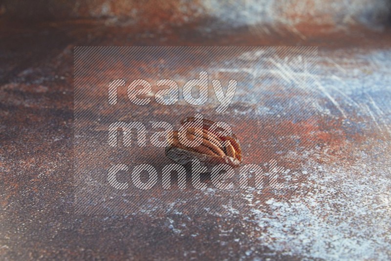 one pecan stuffed madjoul date on a rustic reddish background