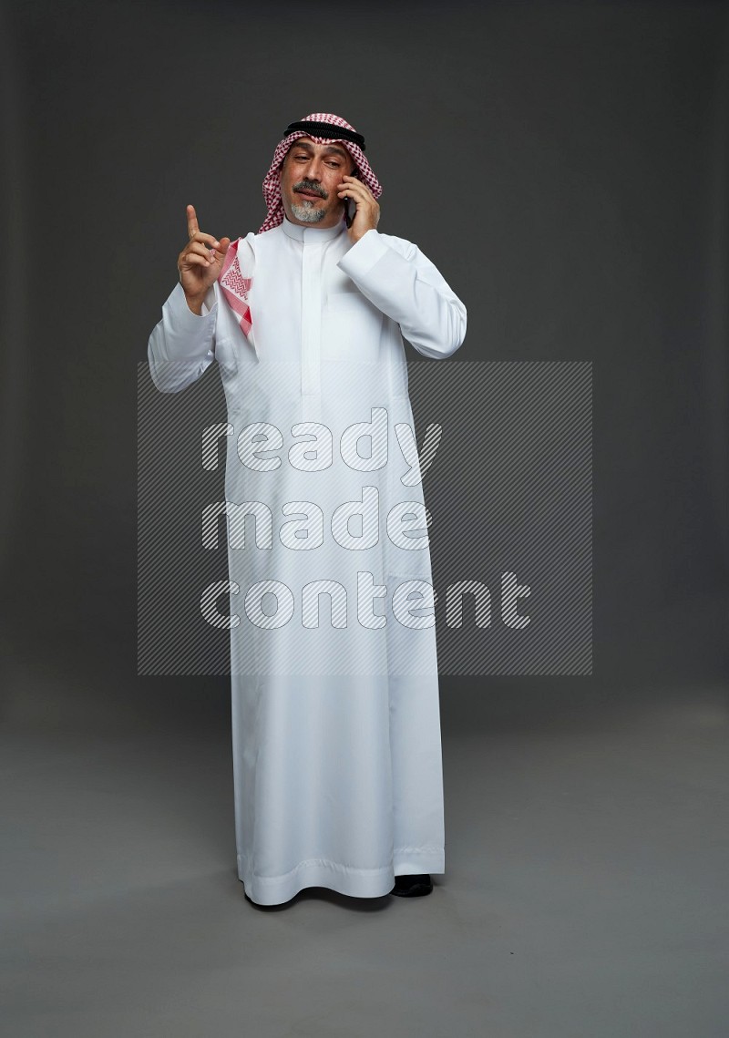 Saudi man with shomag Standing talking on phone on gray background