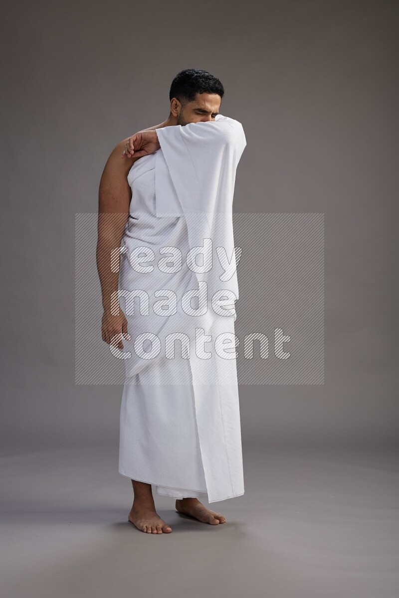 A man wearing Ehram standing showing how to sneeze on gray background