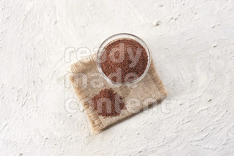 A glass bowl full of garden cress seeds on a burlap fabric on textured white flooring