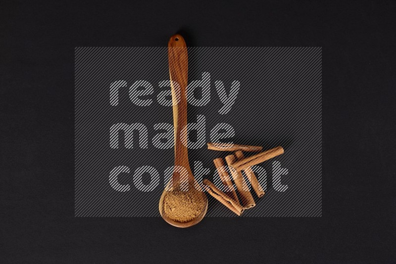 Cinnamon powder in a wooden ladle spoon beside it cinnamon sticks on the flooring on black background in different angles
