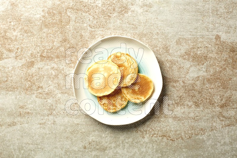 Four stacked plain mini pancakes in a bicolor plate on beige background