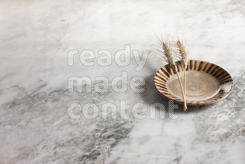 Wheat stalks on multicolored pottery plate on grey marble background
