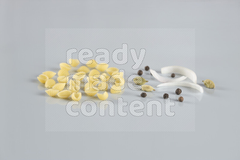 Raw pasta with different ingredients such as cherry tomatoes, garlic, onions, red chilis, black pepper, white pepper, bay laurel leaves, rosemary, cardamom and mushrooms on light blue background