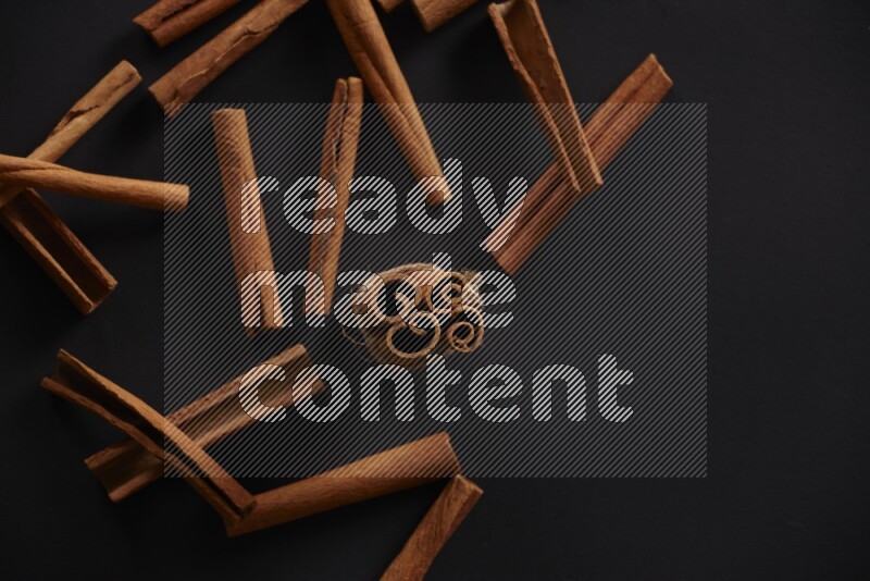 4 Cinnamon sticks stacked and bounded with more sticks in the background on black flooring