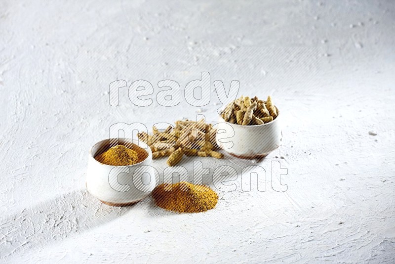 2 beige pottery bowls full of turmeric powder and dried turmeric whole fingers with powder and fingers next of it textured white flooring