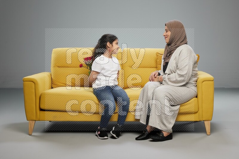 A girl sitting hiding flowers behind her back for her mother on gray background