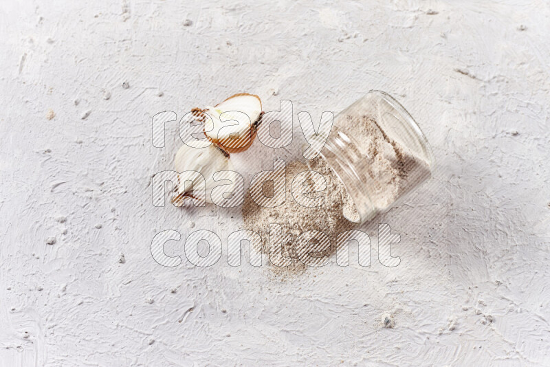 A glass jar full of onion powder flipped with some spilling powder on white background