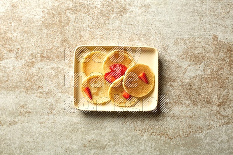 Five stacked strawberry mini pancakes in a rectangular plate on beige background
