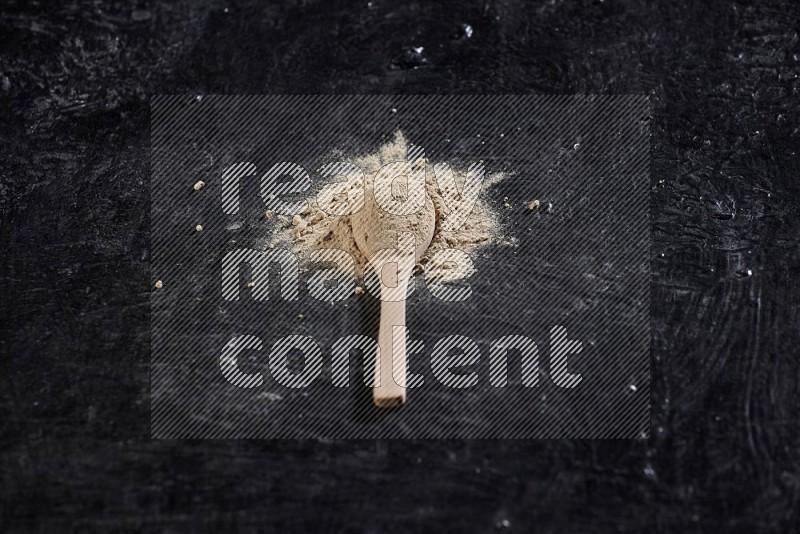 A wooden spoon full of garlic powder surrounded by the powder on a textured black flooring in different angles