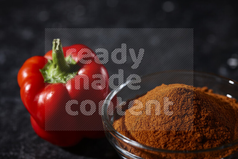 A glass bowl full of ground paprika powder on black background