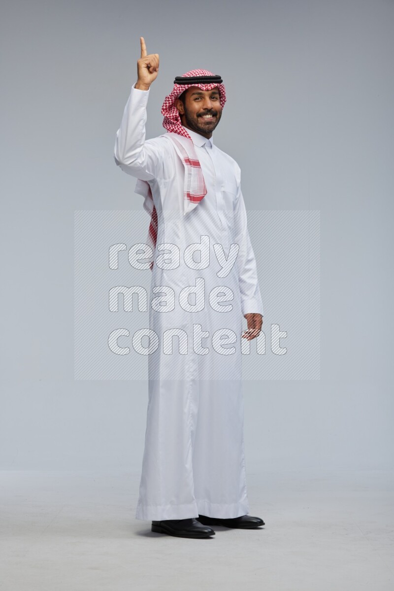 Saudi man Wearing Thob and shomag standing interacting with the camera on Gray background