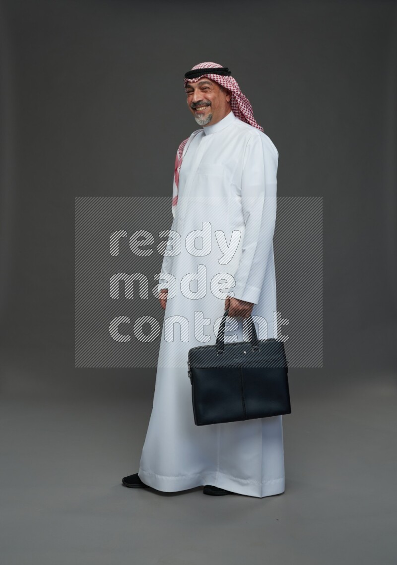 Saudi man with shomag Standing holding bag on gray background