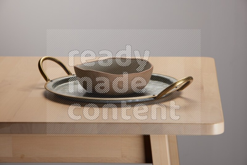 multicolored bowl placed on a rounded stainless steel tray with golden handels on the edge of wooden table