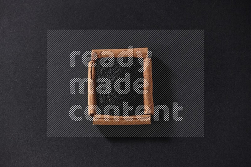 A single square of cinnamon sticks full of black seeds on black flooring