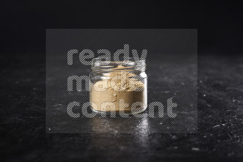 A glass jar full of ground ginger powder on black background