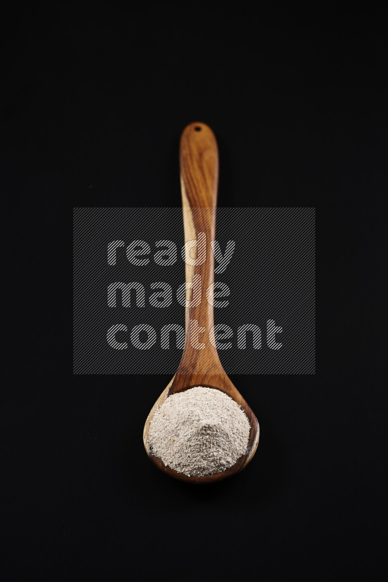 A wooden ladle full of onion powder on black background