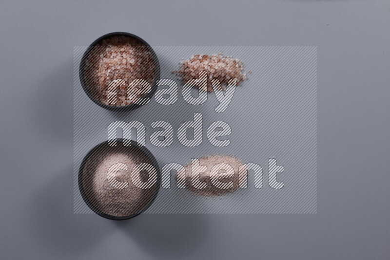 2 pottery bowls one is filled with fine himalayan salt and the other with coarse himalayan salt on grey background