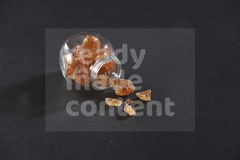 A glass spice jar full of gum arabic and jar is flipped with fallen gum on black flooring in different angles