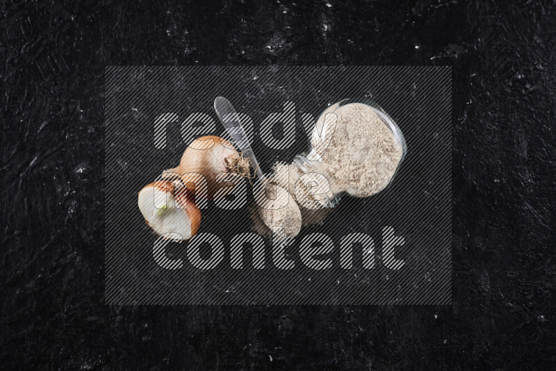 A glass jar full of onion powder flipped with some spilling powder on black background