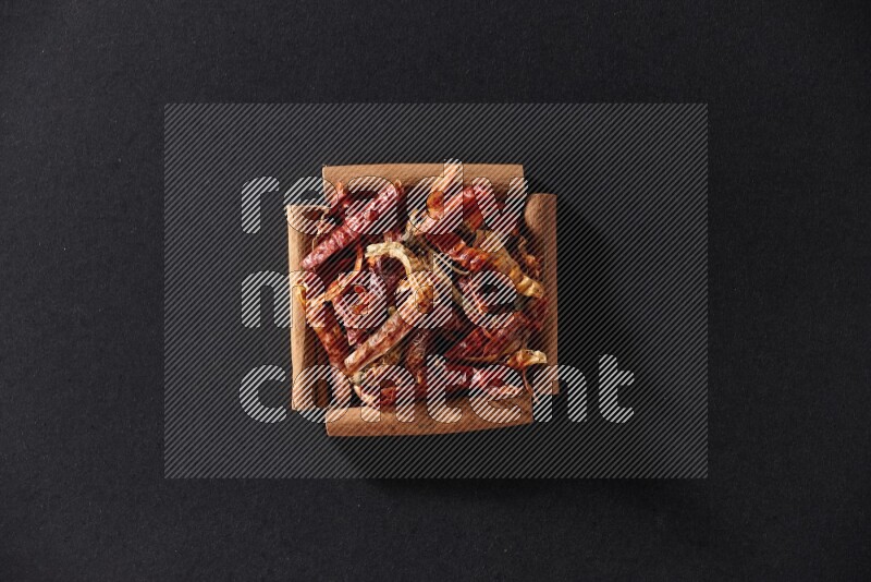 A single square of cinnamon sticks full of chilis on black flooring