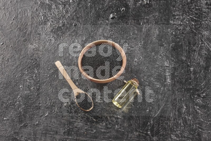 وعاء خشبي وملعقة خشبية ممتلئان ببذور حبة البركة مع زجاجة من زيت حبة البركة علي خلفية سوداء