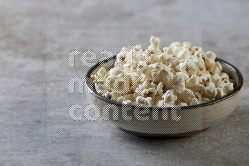 popcorn in a multi-colored pottery bowl on a grey textured countertop