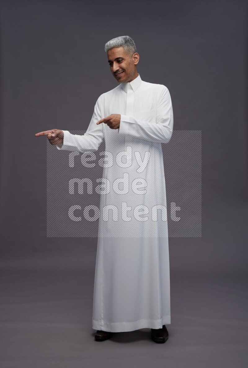 Saudi man wearing thob standing interacting with the camera on gray background