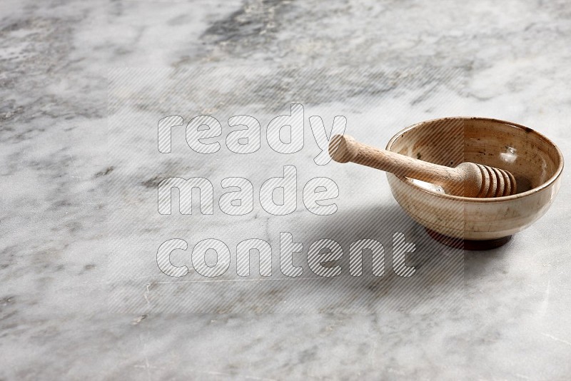 Beige Pottery Bowl with wooden honey handle in it, on grey marble flooring, 45 degree angle