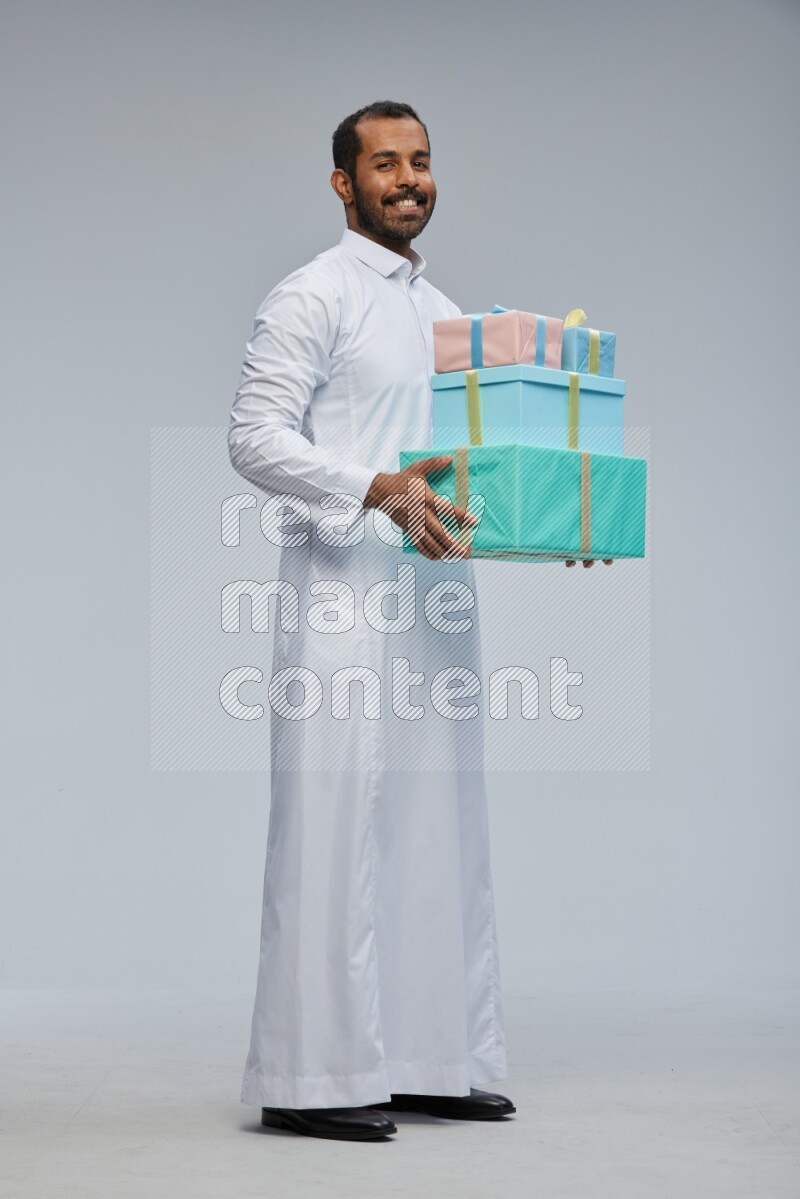 Saudi man Wearing thob standing holding gift box on Gray background