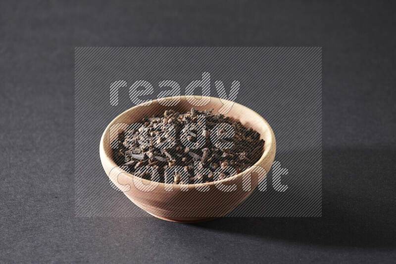 A wooden bowl full of cloves on a black flooring