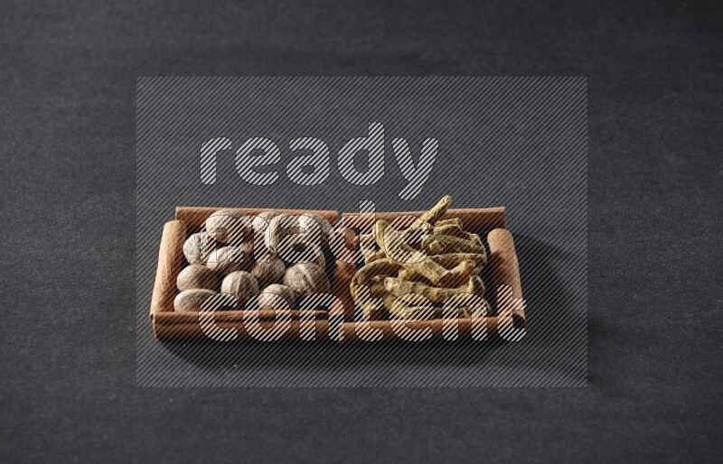 مربعان من أعواد القرفة ممتلئان بجوزة الطيب وأصابع الكركم علي خلفية سوداء