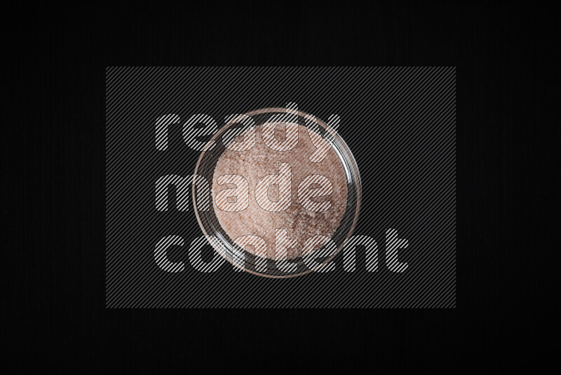 A glass bowl full of fine himalayan salt on black background