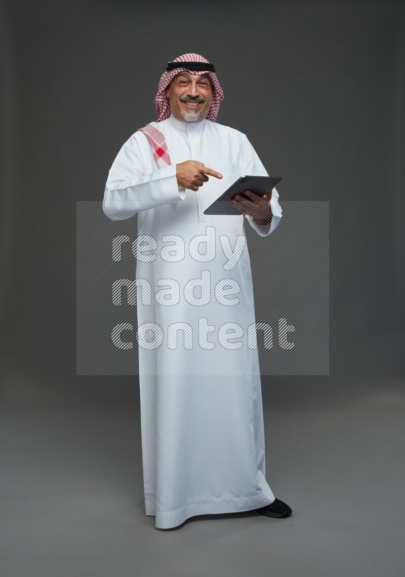 Saudi man with shomag Standing working on tablet on gray background