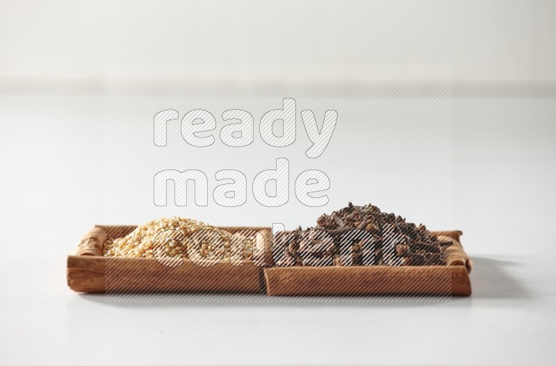 مربعان من أعواد القرفة ممتلئان بالقرنفل وبذور السمسم علي خلفية بيضاء