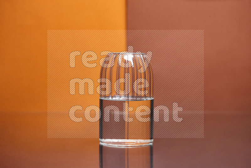 The image features a clear glassware filled with water, set against orange and dark orange background