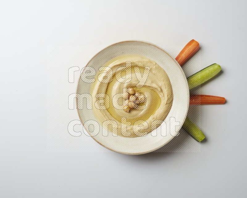 Hummus in a pottry plate garnished with roasted chickpeas on a white background