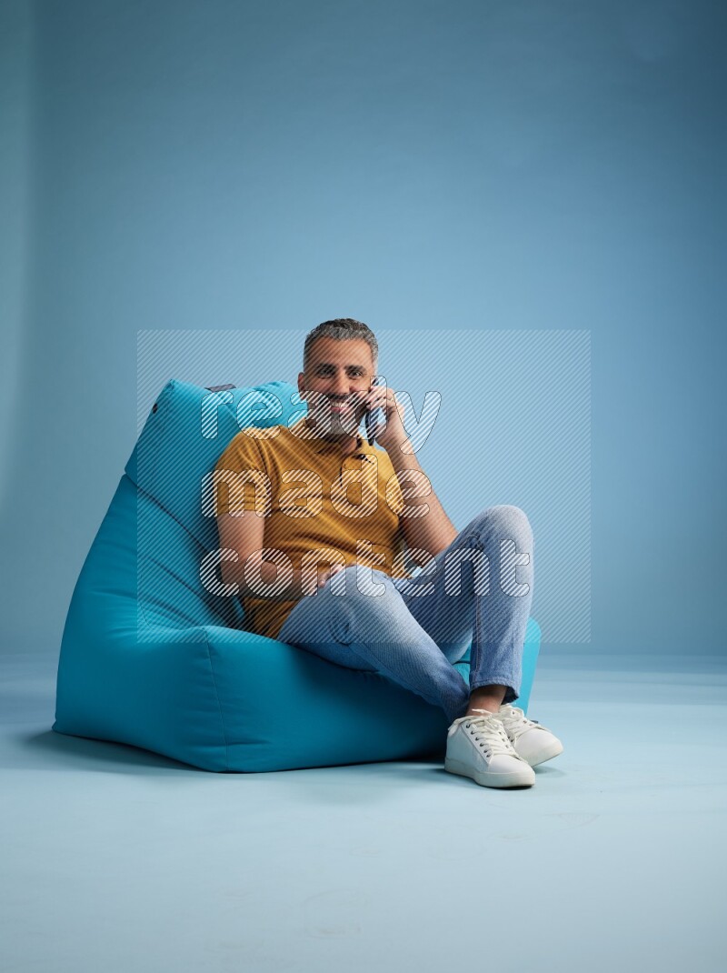 A man sitting on a blue beanbag and talking on the phone