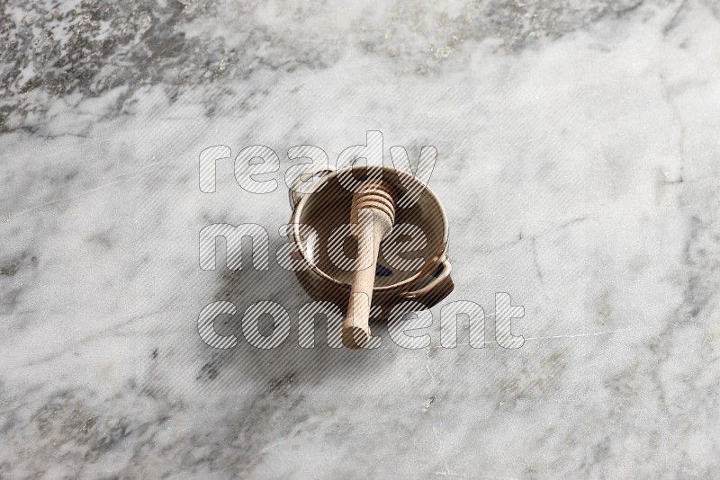 Multicolored Pottery bowl with wooden honey handle in it, on grey marble flooring, 65 degree angle