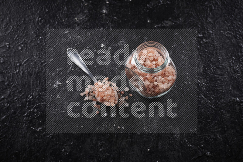 A glass jar full of coarse himalayan salt crystals on black background