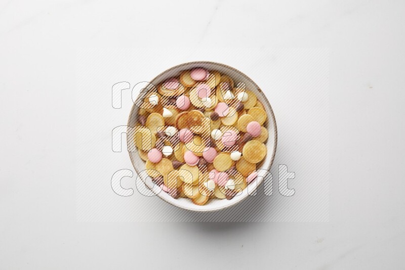 Top-view shot of mixed chocolate chips cereal pancakes in a round bowl on white background