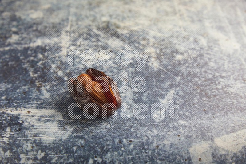 one almond stuffed madjoul dates on a rustic blue background