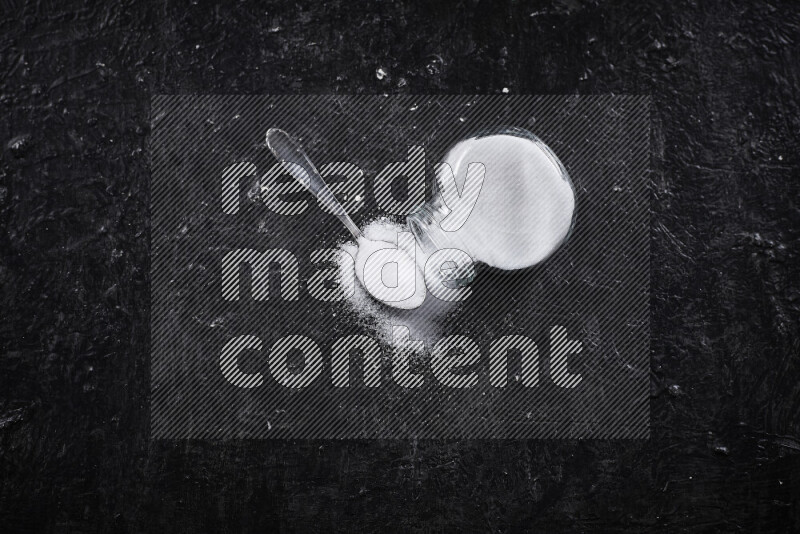 A glass jar full of fine table salt on black background