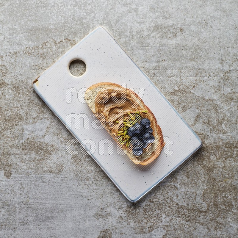 open faced peanut butter sandwich with blueberries and pistachio on a grey textured background
