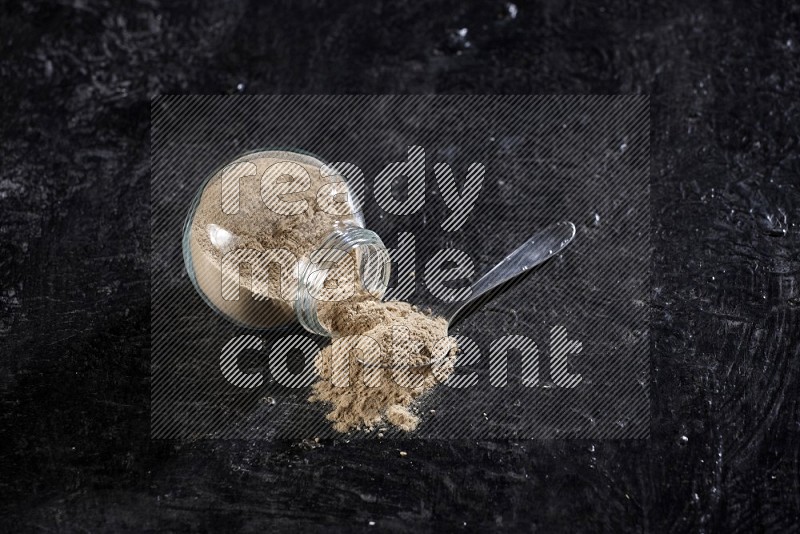 A glass spice jar full of garlic powder flipped and the powder came out with metal spoon on a textured black flooring in different angles